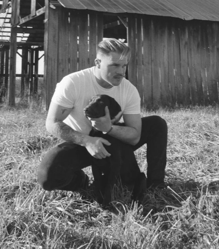 a man kneeling down holding a baby in front of an old wooden building with a barn in the background