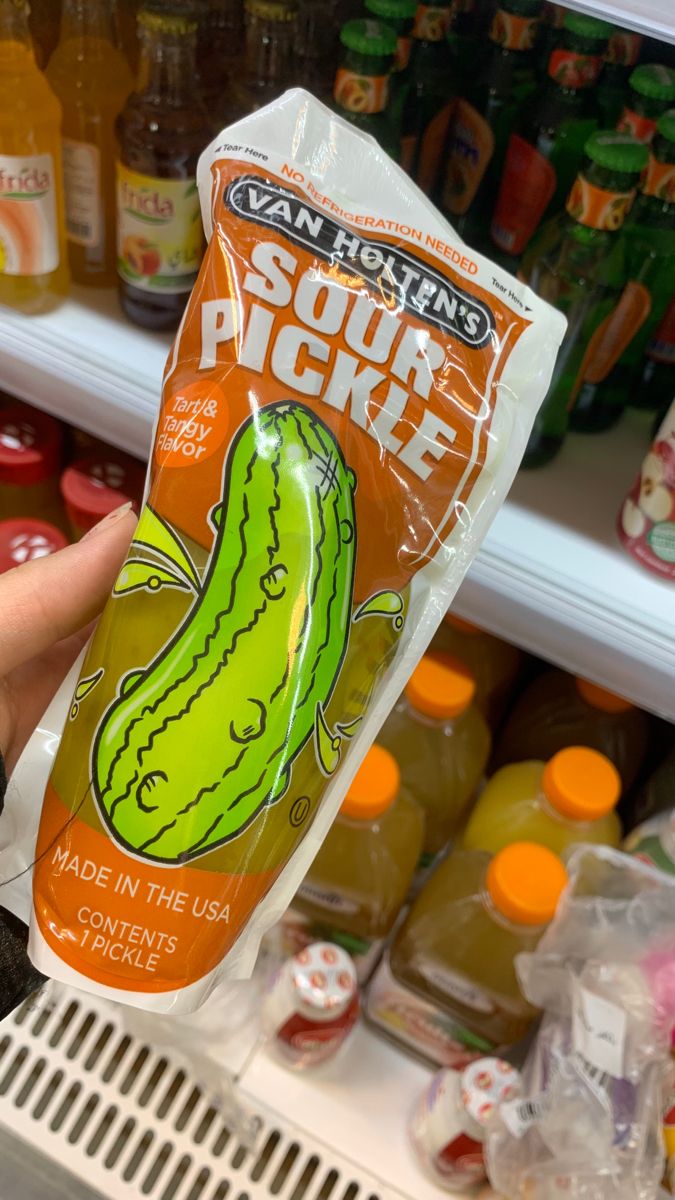 someone holding up a bag of sour pickle in front of a refrigerator filled with drinks