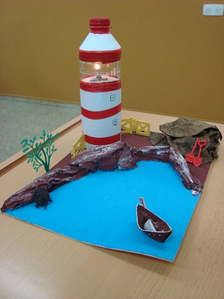 a paper model of a lighthouse on a table next to a plastic bottle and boat