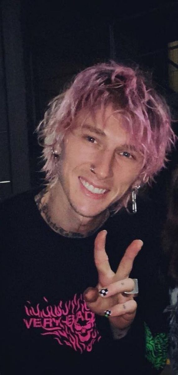 a man with pink hair and piercings making the v sign while standing next to another person