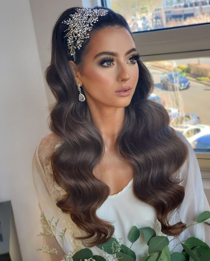 a woman with long brown hair wearing a tiara and holding a flower in front of a window