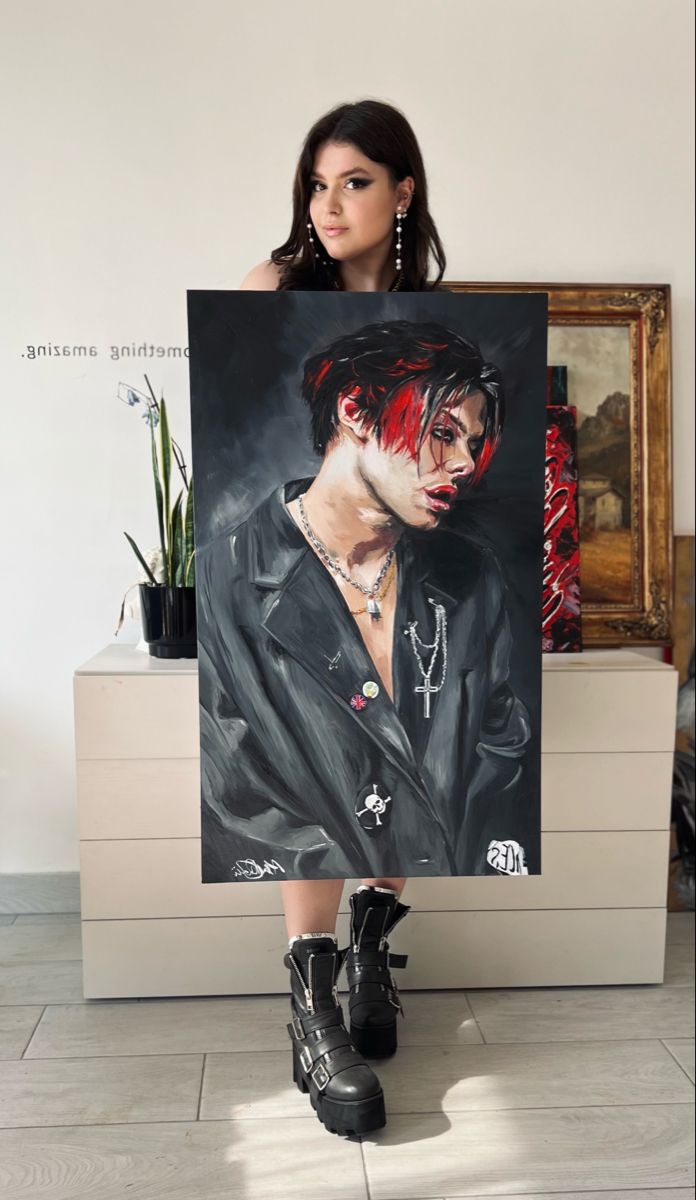 a woman standing next to a painting of a man with red hair and piercings