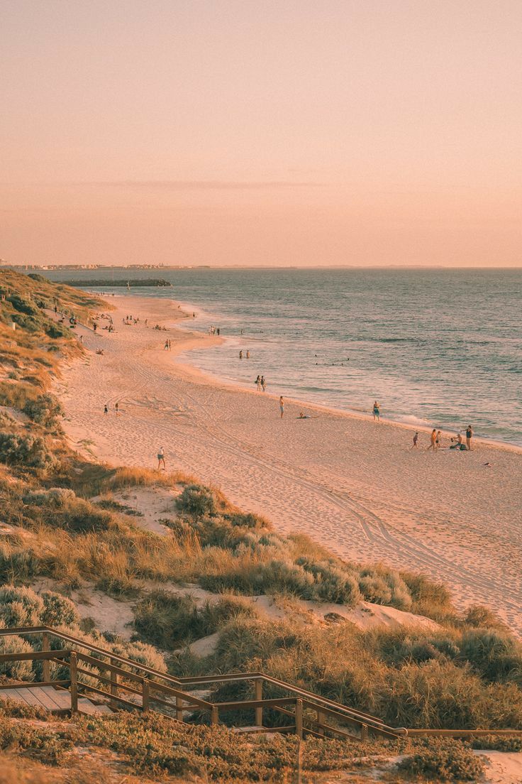 people are walking on the beach at sunset