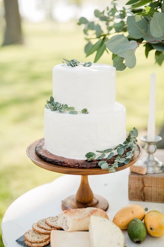 a white cake sitting on top of a wooden table next to fruit and crackers