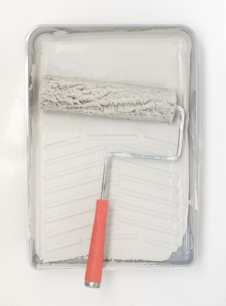 a paint roller sitting on top of a white tray next to a red brush in it