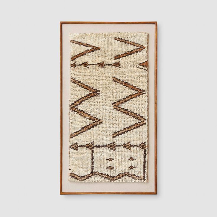 an old rug hanging on the wall in front of a white wall with a wooden frame