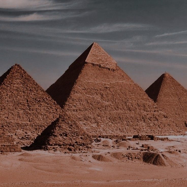 three pyramids in the desert under a cloudy sky