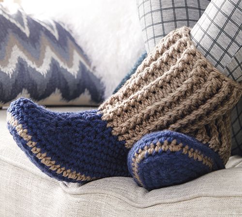 a person's feet wearing socks and slippers on a couch next to pillows