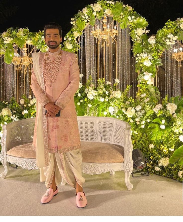 a man standing next to a white bench in front of a flower covered wall with chandeliers