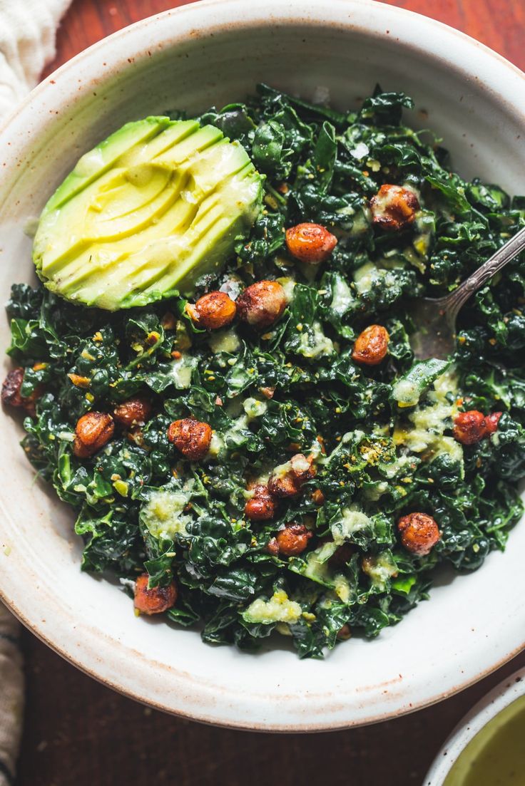 a bowl filled with spinach and avocado on top of a wooden table