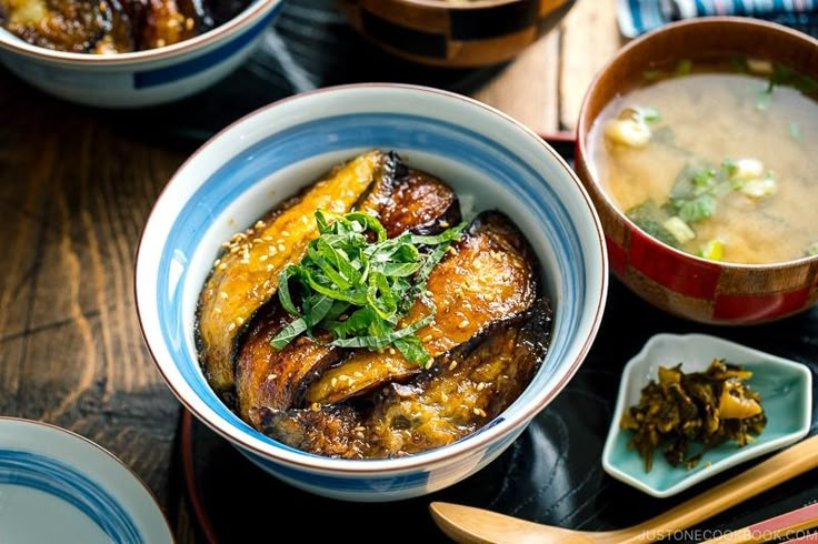 bowls of food on a table with chopsticks and spoons next to them