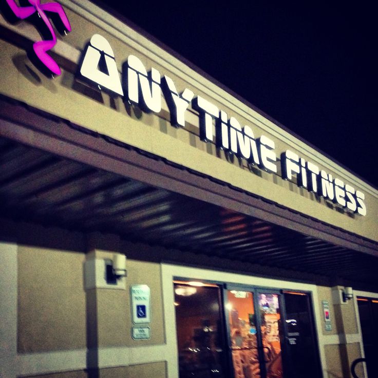 the entrance to an anytime fitness store lit up at night with neon pink letters on it