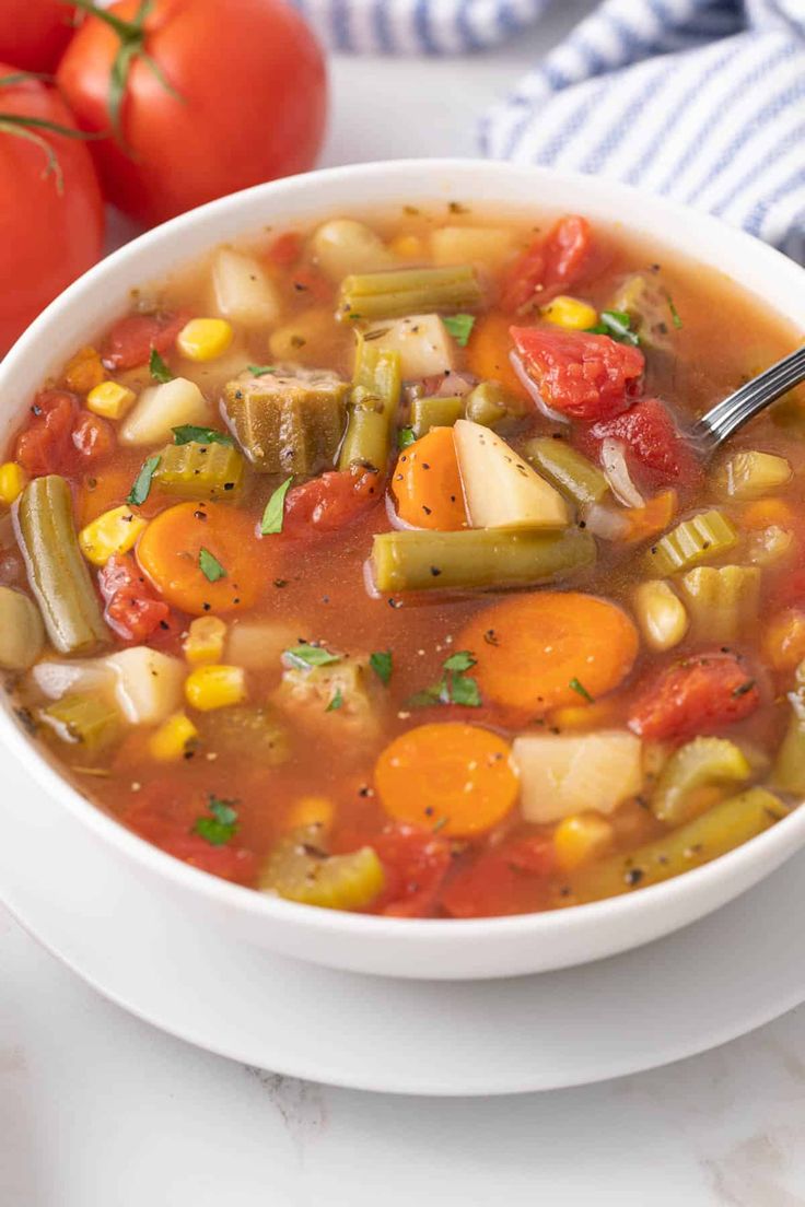 a white bowl filled with vegetable soup next to tomatoes