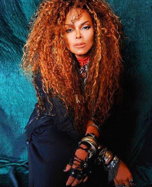 a woman with long red hair sitting on a blue cloth covered chair and posing for the camera