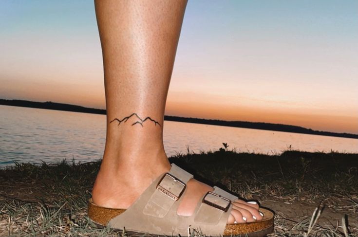 a woman's foot with a small tattoo on her left side and mountains in the background