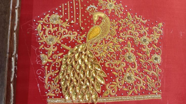 a red and gold embroidered piece with a peacock on it's back, in front of a wooden frame