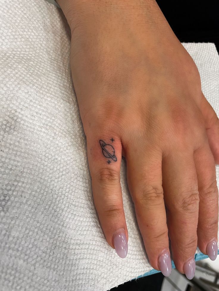 a woman's hand with a small saturn tattoo on her left thumb and finger