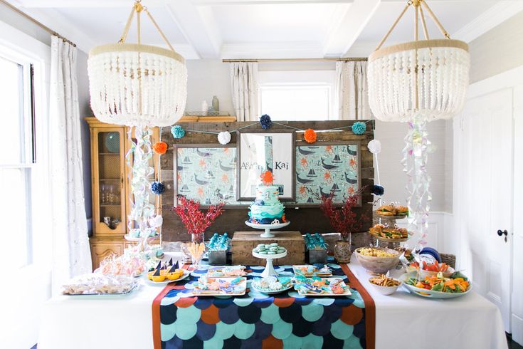 a table topped with lots of food next to a window covered in balloons and streamers