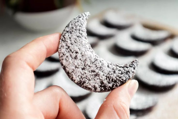 a person holding up a half eaten cookie in front of some cookies on a table