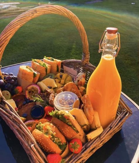 a picnic basket filled with sandwiches and fruit next to a bottle of orange juice on a table