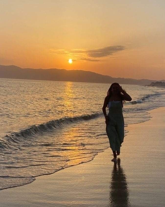 a woman walking on the beach at sunset