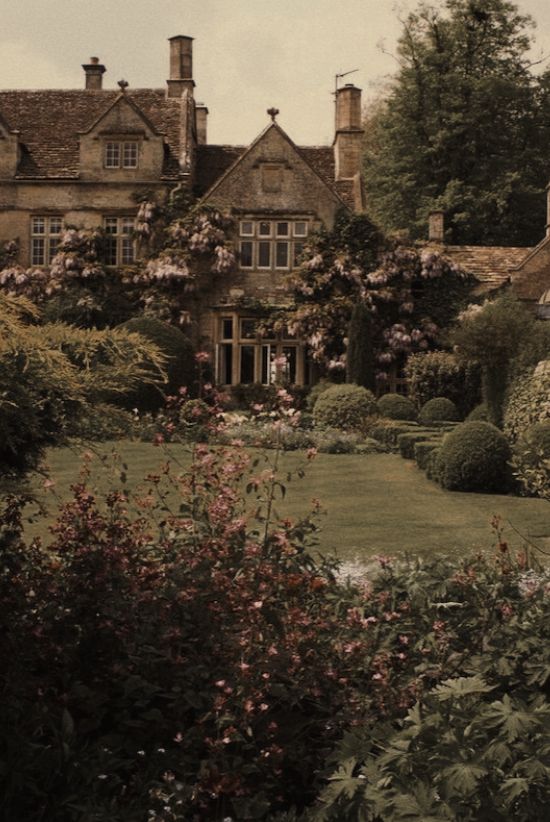 an old house with lots of flowers in the front yard and bushes on either side