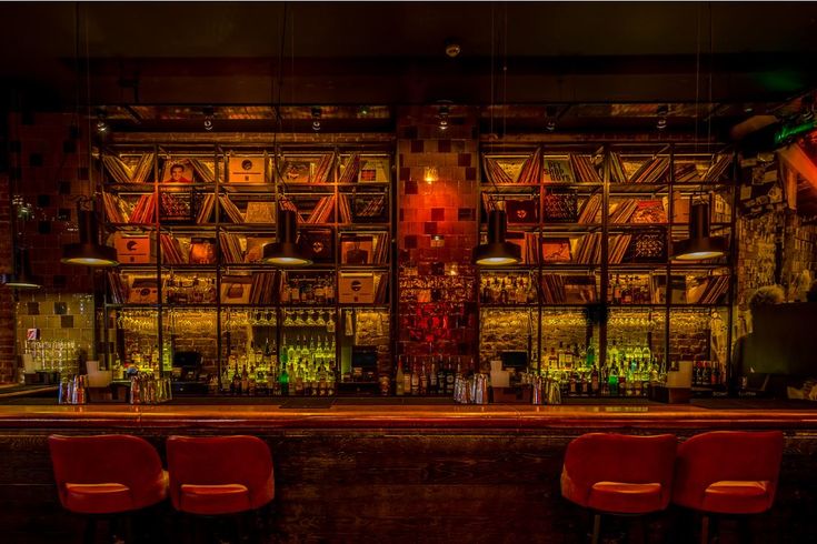 an empty bar with red chairs in front of the bar and shelves full of books