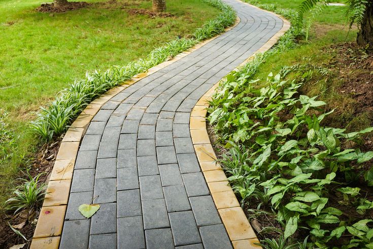 a brick path in the middle of a garden with green grass and trees behind it