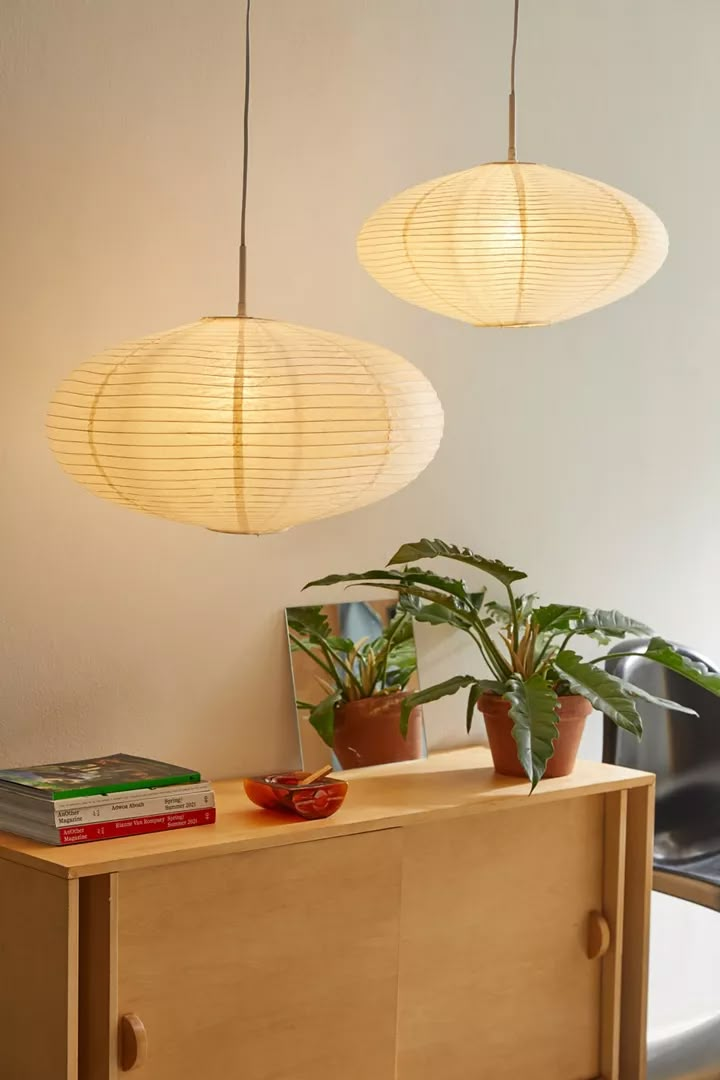 two lamps hanging from the ceiling above a wooden cabinet with books on it and a potted plant