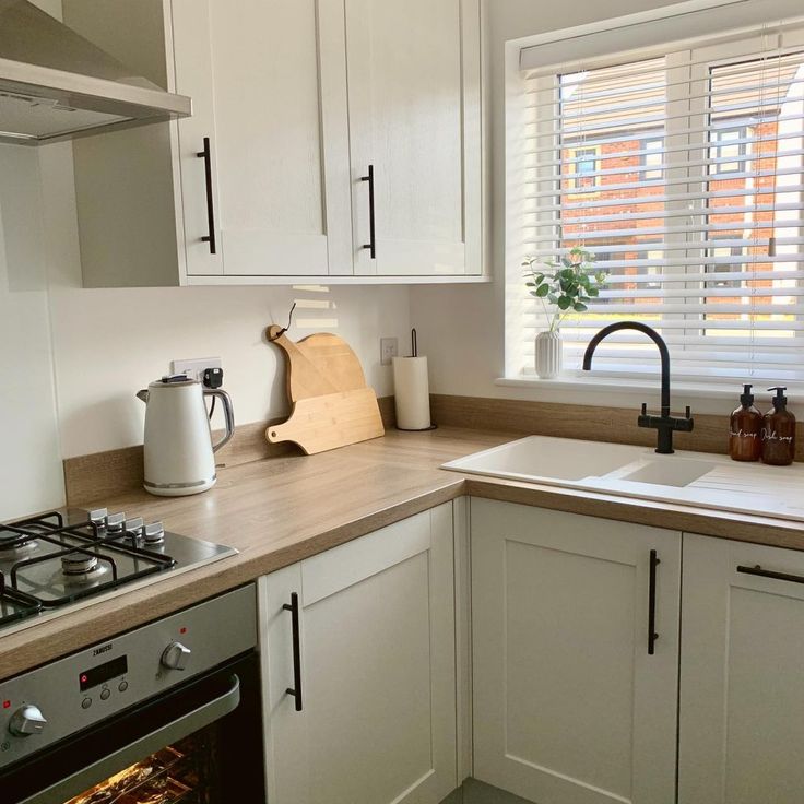 a kitchen with white cupboards and wooden counter tops, an oven door is open in front of the window