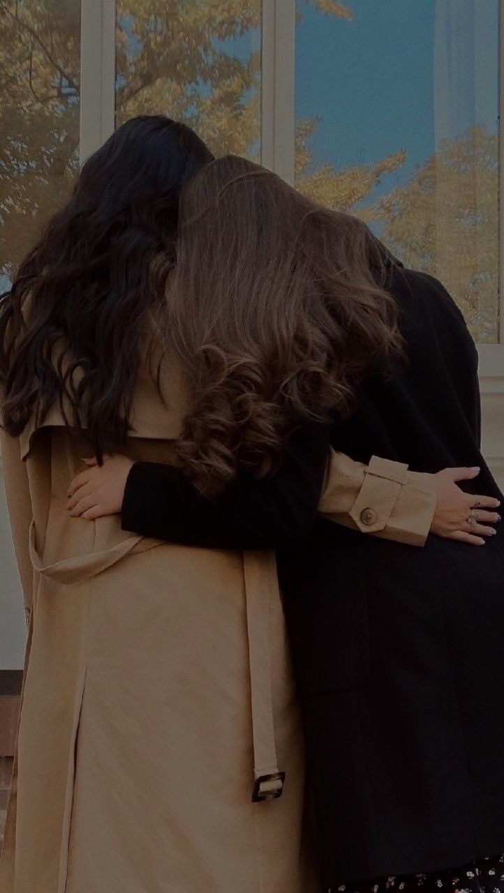 two women hugging each other in front of a window