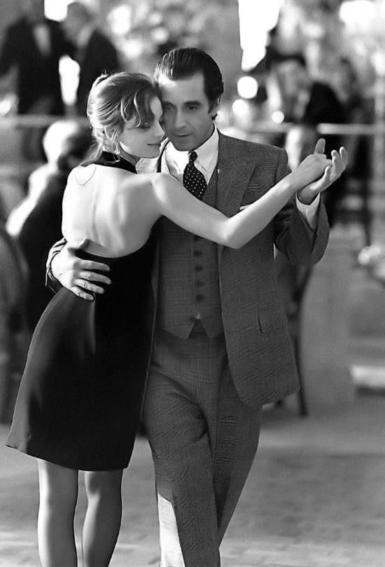 a man in a suit and tie is hugging a woman's neck as they walk down the street