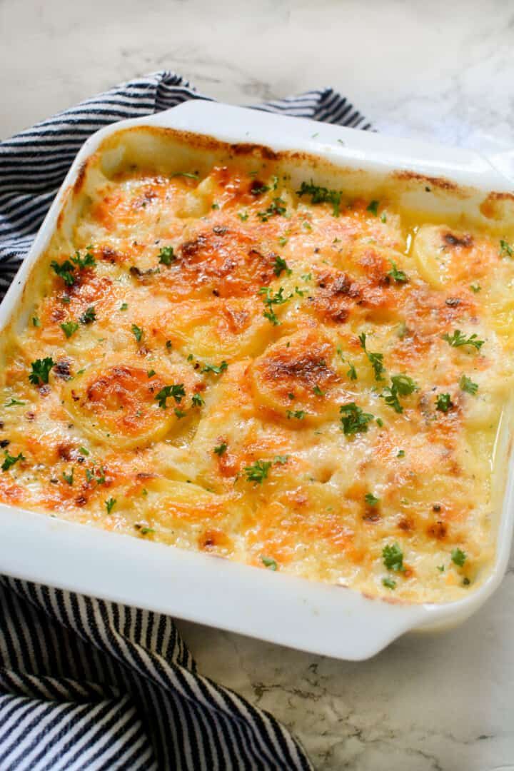 a casserole dish with cheese and parsley in it on a striped cloth