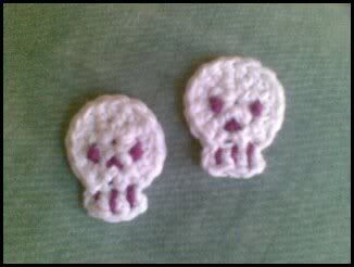 two crocheted skulls sitting next to each other on a green tablecloth covered surface