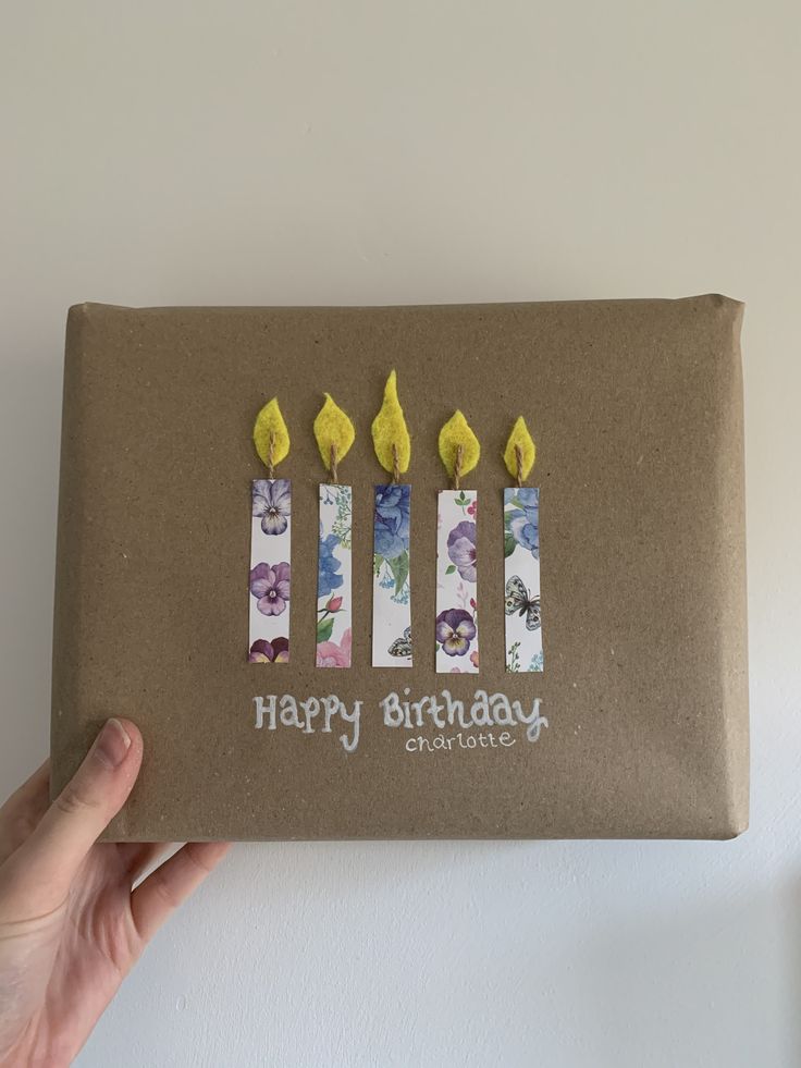 a hand holding a brown birthday card with four lit candles on it's side