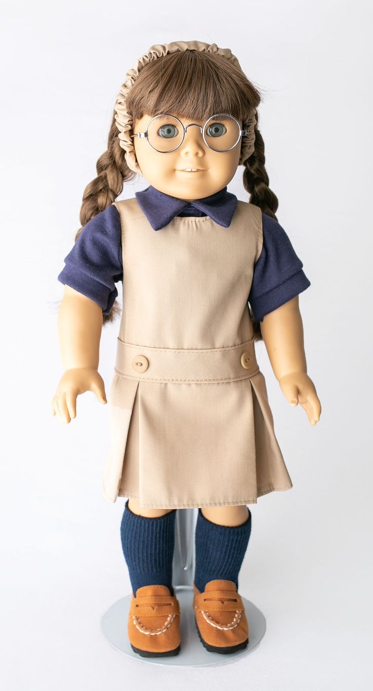 the doll is wearing glasses and a tan dress with blue sleeves, brown shoes, and long hair