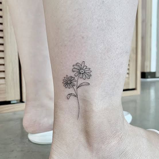 a small flower tattoo on the ankle that is black and white with a single daisy