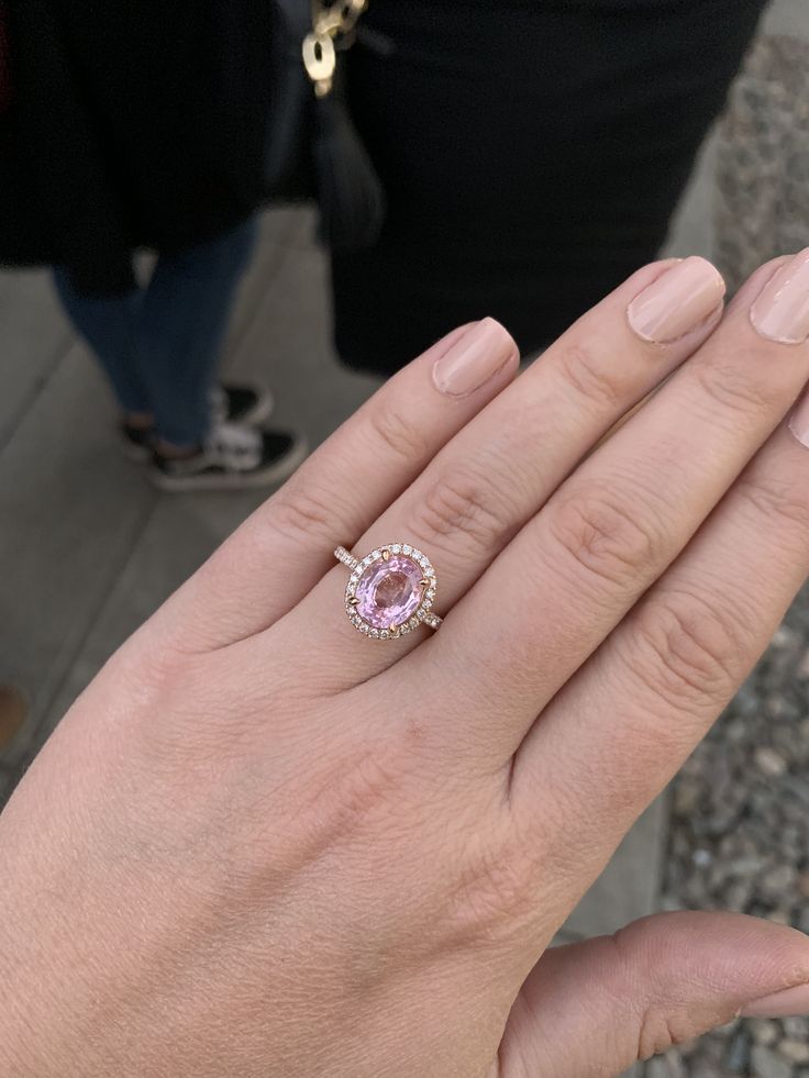 a woman's hand with a pink ring on top of her finger and two other people in the background