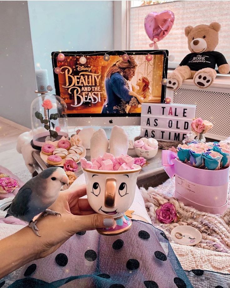 a person holding a cup with pink frosting on it in front of a tv