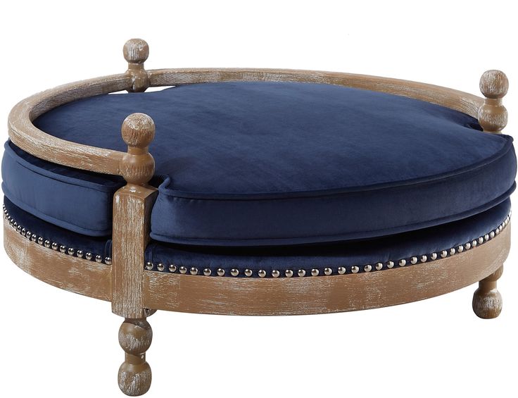 a round wooden ottoman with blue velvet upholstered cushion and nail studded legs