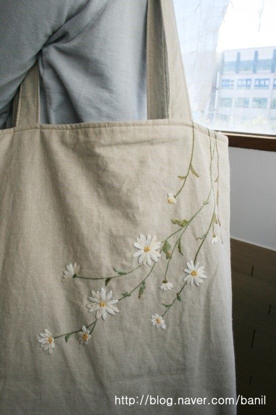 a person holding a white bag with daisies on the front and side, in front of a window