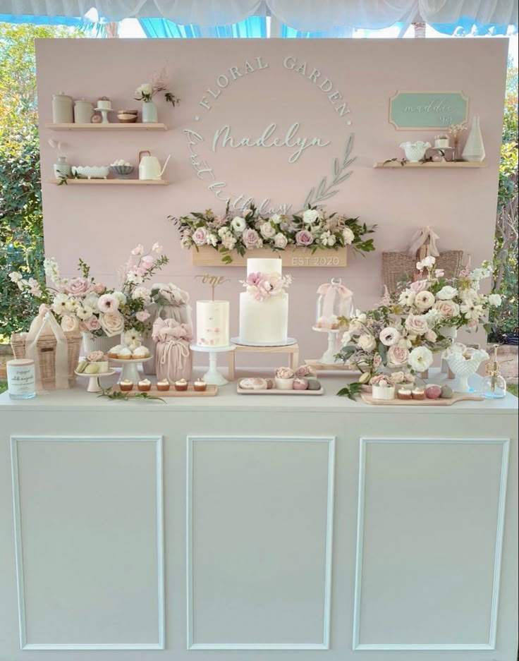 a table topped with lots of cakes and desserts next to a wall covered in flowers