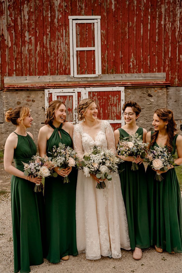 a group of women standing next to each other in front of a red barn holding bouquets