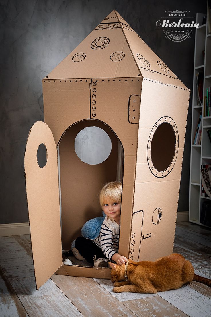 a little boy sitting in a cardboard house with a cat