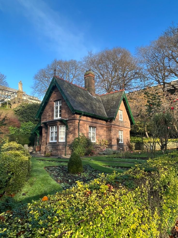 a brick house with a green roof surrounded by trees and bushes in the foreground