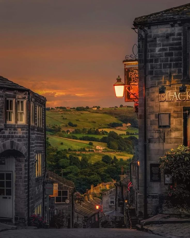 the sun is setting over an old town with stone buildings and green hills in the background