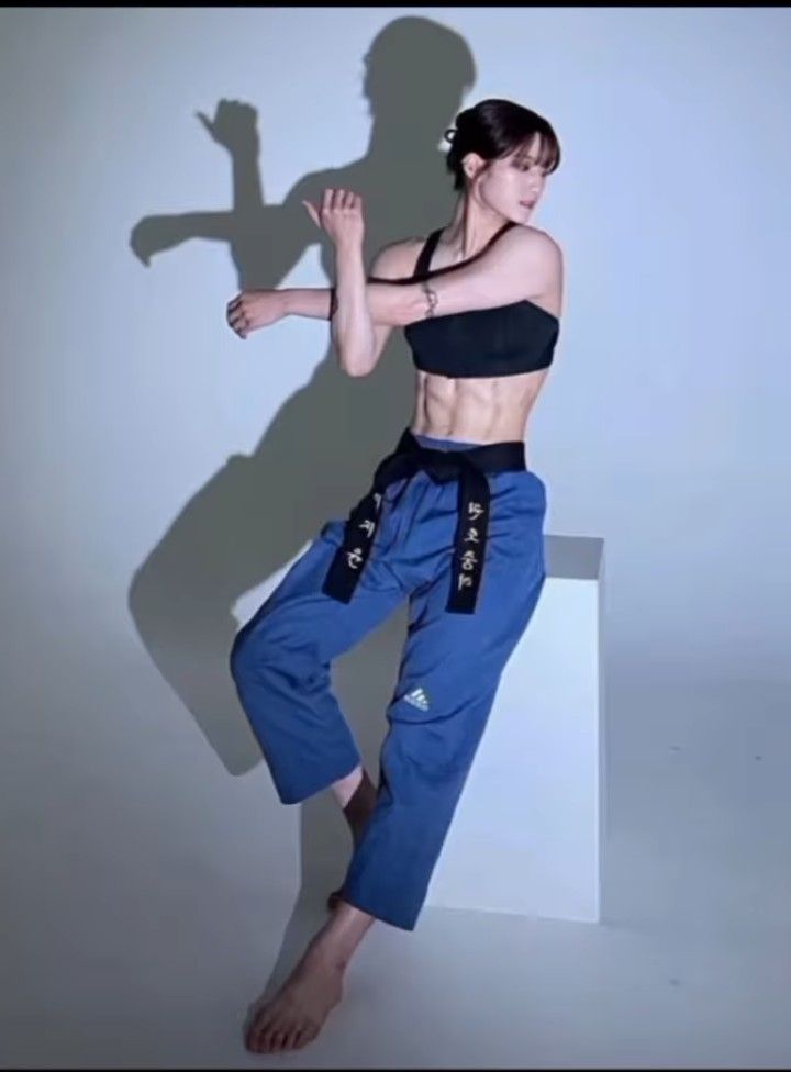 a woman in blue pants and black top posing for a photo with her shadow on the wall