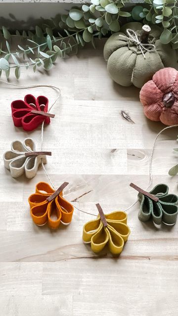 several small pieces of fabric hanging from strings on a white surface with greenery in the background