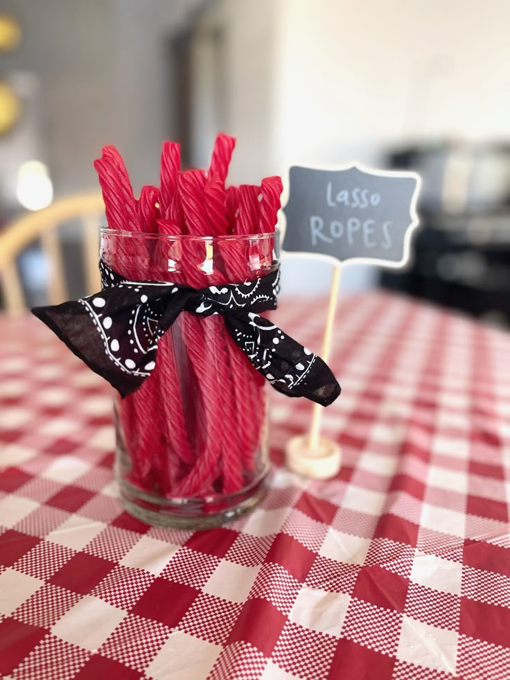 some red and white straws are in a glass on a checkered table cloth