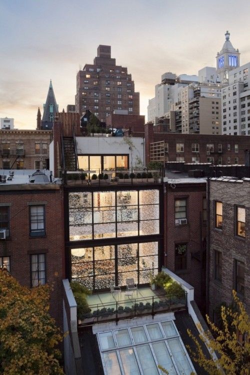 an apartment building with lots of windows and plants on the roof, surrounded by tall buildings